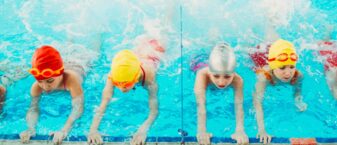 Des enfants dans une piscine sont accrochés au rebord et apprennent à battre des pieds sous l'eau.