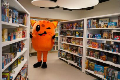 La mascotte de la Ville, le chat orange Tillon, fait un pouce dans les rayons de la ludothèque - Agrandir l'image, fenêtre modale