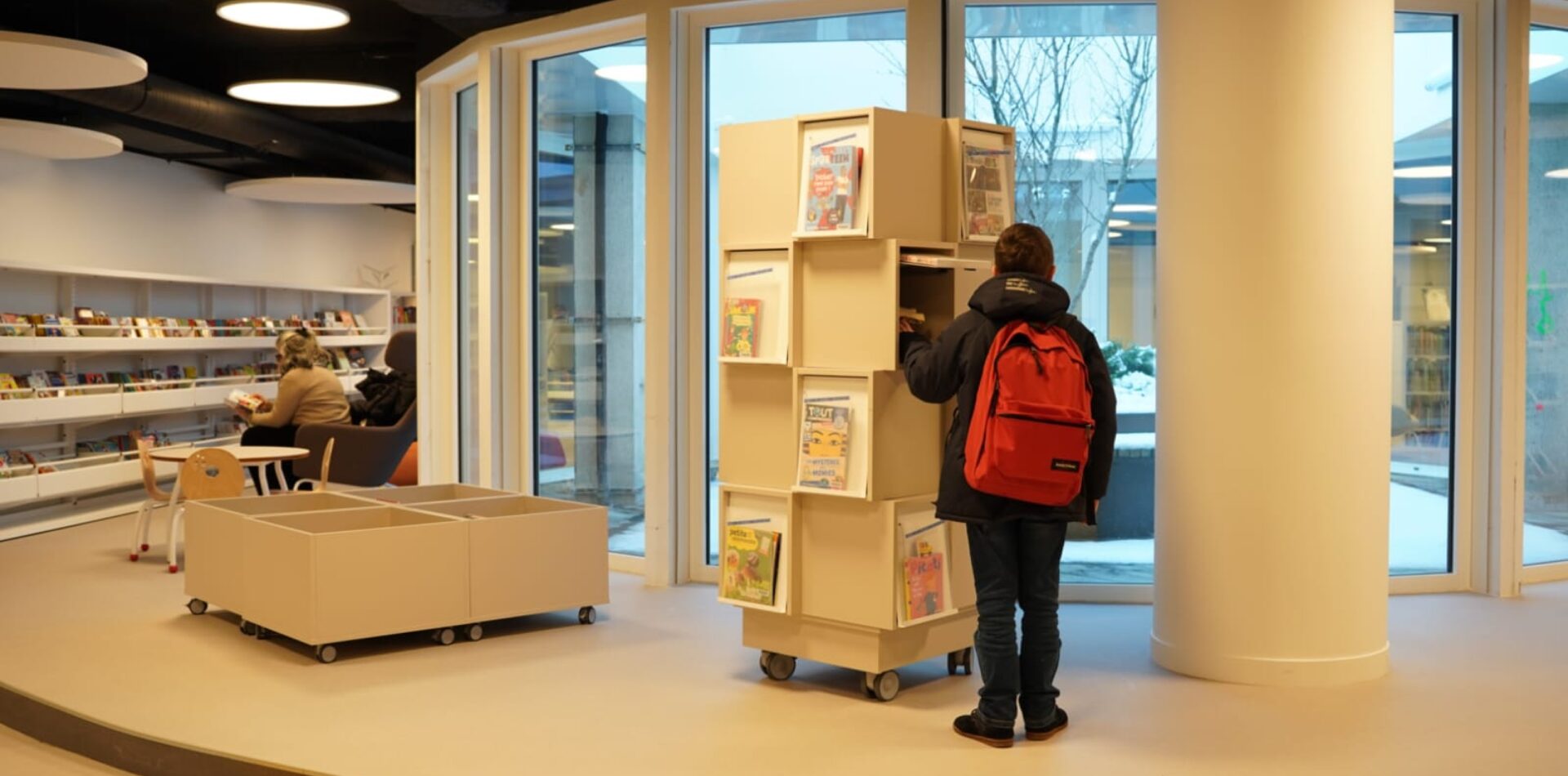 Un enfant avec un cartable rouge choisit un livre sur les étals de la nouvelle ludo-médiathèque de Châtillon.