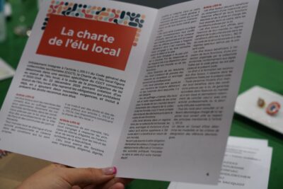 Gros plan sur un livret ouvert intitulé « La charte de l’élu local », tenu en main, présentant les principes et obligations des élus avec un contenu réglementaire détaillé. - Agrandir l'image 2 sur 9, fenêtre modale