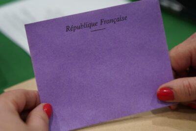 Gros plan sur un bulletin de vote violet portant la mention « République Française », tenu entre deux mains, lors du scrutin organisé pendant la séance d’installation du Conseil municipal. - Agrandir l'image 4 sur 9, fenêtre modale