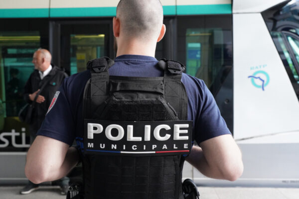 Un agent de la Police municipale est vu de dos, portant un gilet avec l’inscription « Police municipale », devant une rame de tramway à l’arrêt. Un autre homme se tient à proximité sur le quai.