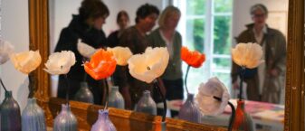 Oeuvres de l'exposition cire(s) posées sur une cheminé. Ce sont des fleurs en cires dans des vases en cire.