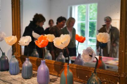 Oeuvres de l'exposition cire(s) posées sur une cheminé. Ce sont des fleurs en cires dans des vases en cire. - Agrandir l'image, fenêtre modale