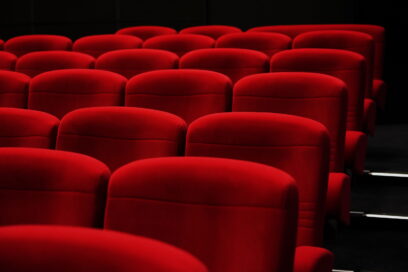 Rangées de fauteuils rouges d'une salle de cinéma, vues en légère plongée. Les sièges vides se détachent sur un fond sombre, évoquant une projection à venir dans une ambiance calme et confortable. - Agrandir l'image, fenêtre modale