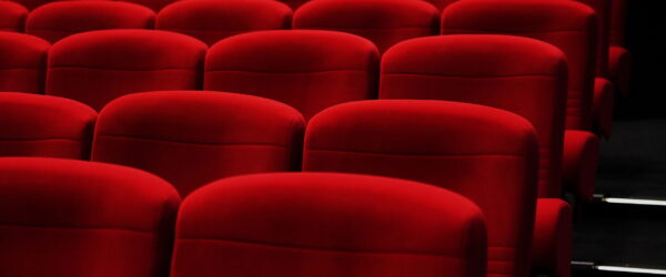 Rangées de fauteuils rouges d'une salle de cinéma, vues en légère plongée. Les sièges vides se détachent sur un fond sombre, évoquant une projection à venir dans une ambiance calme et confortable.