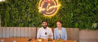 Chef cuisinier et gérante du restaurant The Corner assis côte à côte et présentant leur pizza