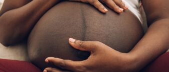 Un gros plan sur le venre d'une femme noire enceinte. Elle tient son ventre entre ses mains.